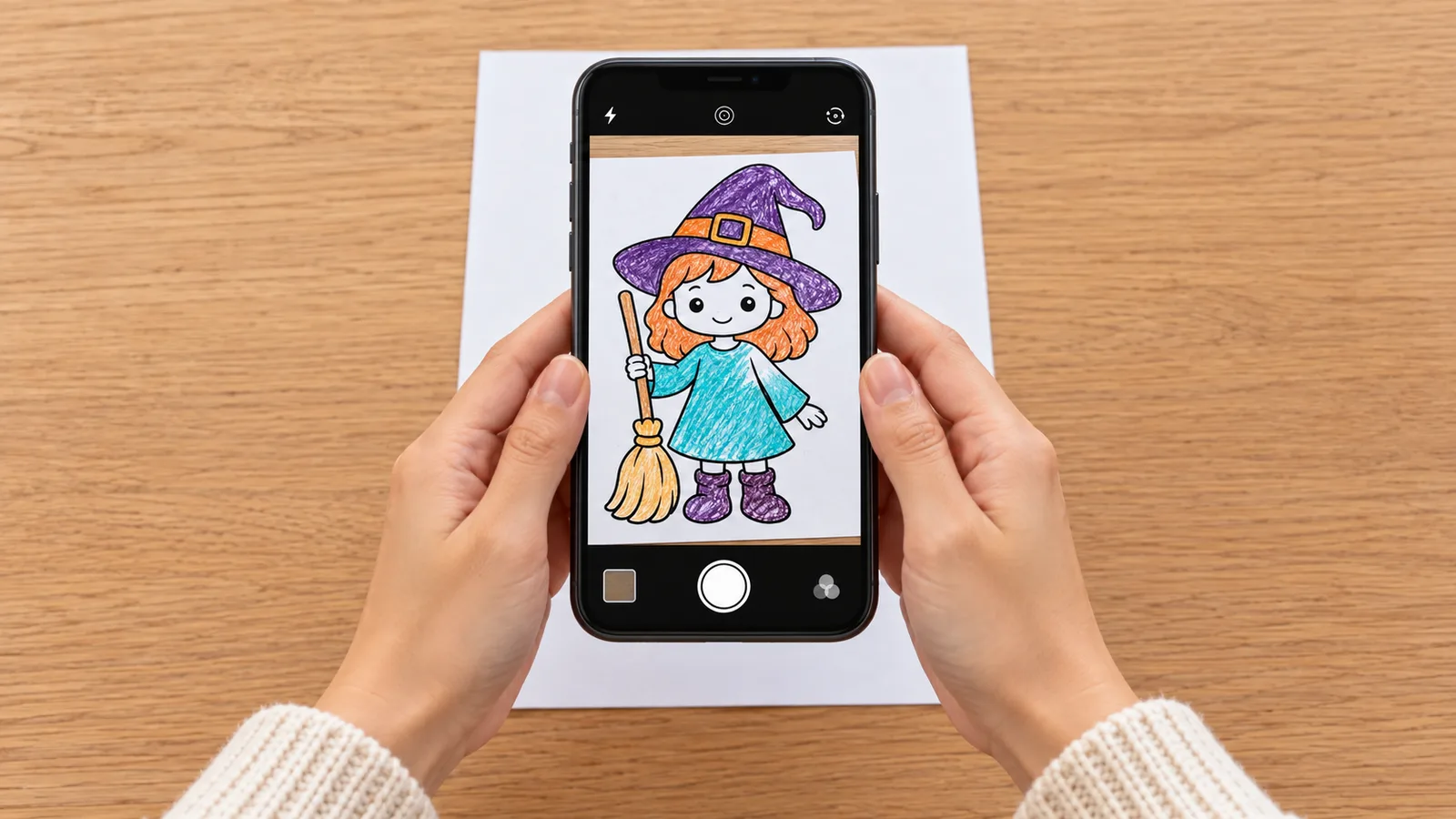 Parent naturally holding an unbranded phone vertically above a colored little witch page, with the drawing visible in a simple camera preview.
